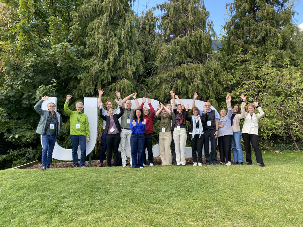 Members of TheRaCil consortium posing and waving (like cilia) in front of University College Dublin sign during the Cilia2024 international conference.